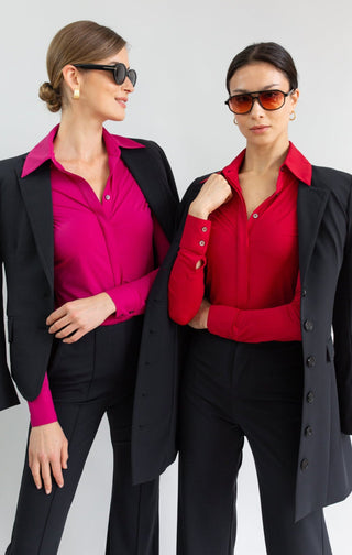 Two women wearing black blazers over pink and red shirts on a white background