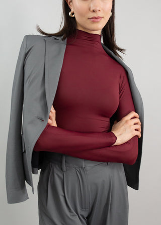 Woman wearing a maroon turtleneck and gray suit jacket against a plain background