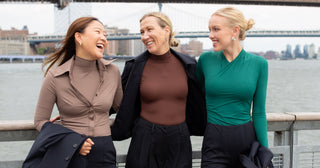 Three women standing together on a bridge with a cityscape in the background