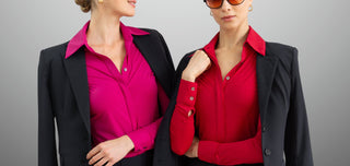 Two women wearing black blazers over pink and red shirts against a gray background