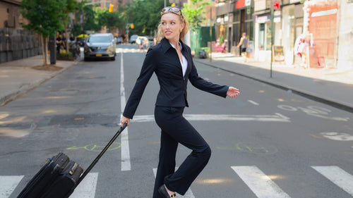 Woman in a suit with a suitcase crossing a street on a zebra crossing