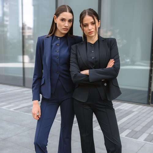 Two women in professional attire standing outdoors with a modern building in the background.