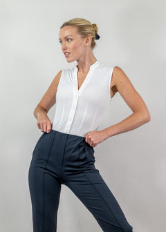 Woman wearing a white blouse and black pants against a plain background