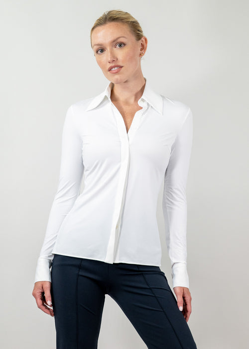 Woman wearing a white blouse and dark pants against a plain background