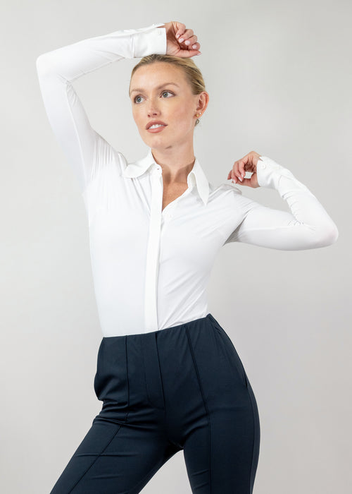 Woman wearing a white blouse and dark pants against a plain background